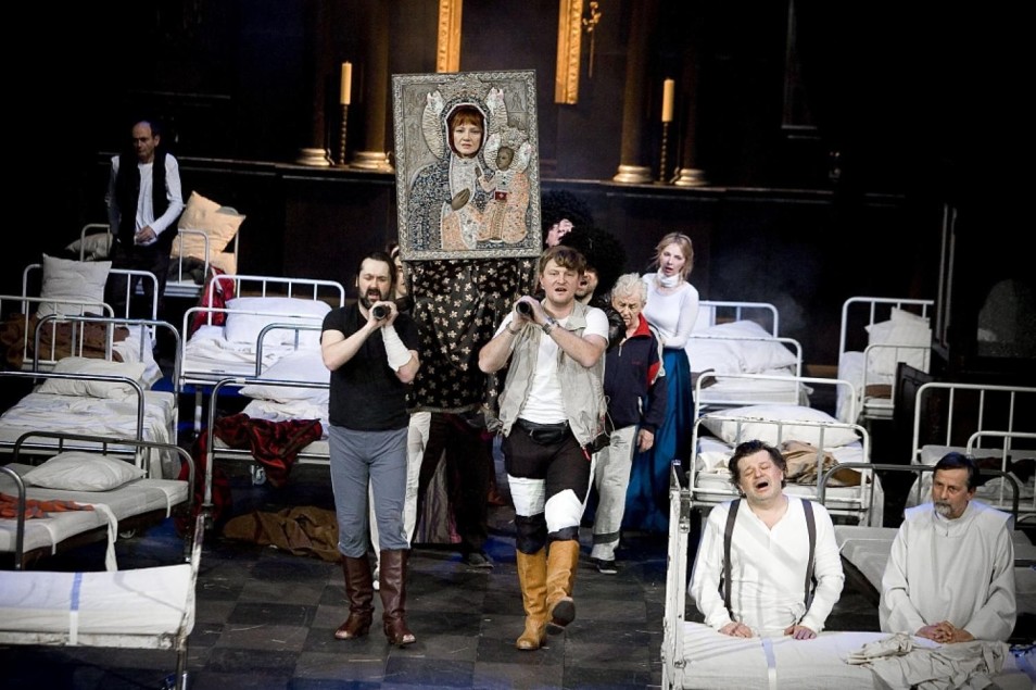 Grupa aktorów maszeruje między łóżkami szpitalnymi, niosąc ikonę Matki Boskiej. Postacie w różnych pozach, scena pełna napięcia i ruchu.