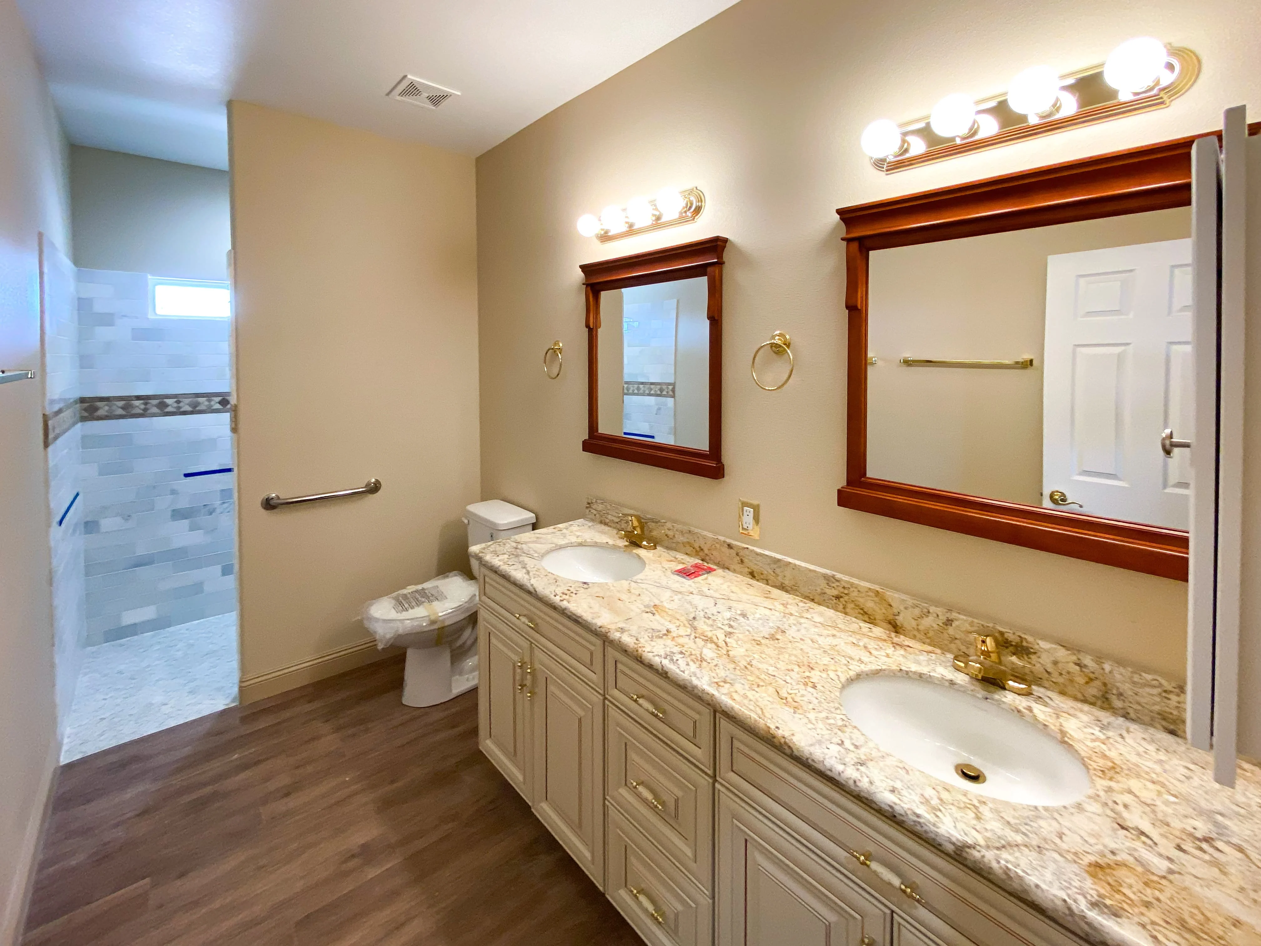 Thoughtfully designed bathroom with dual sinks on granite counter, matching cabinetry, and a walk-in shower with intricate tile work - Custom Home built by James Development Corp. Las Vegas, NV.