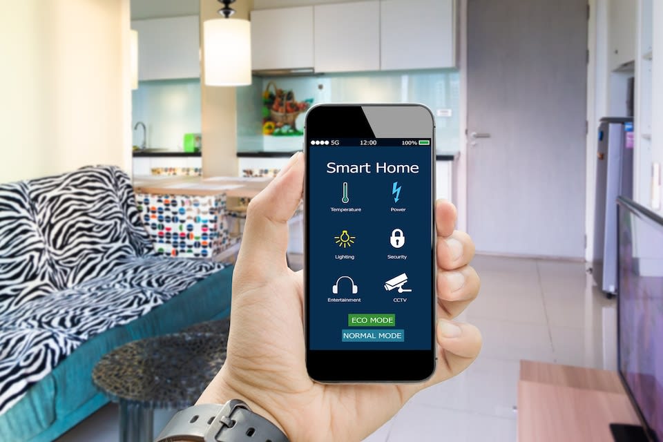 Mains tenant un smartphone avec application maison intelligente sur une chambre floue