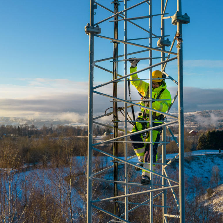 Two men in safety gear standing next to a radio tower.