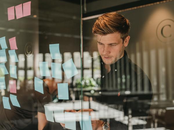 A person looking at a sticky note on a glass wall.