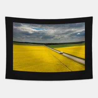 Truck on a road, aerial landscape of a road amongst fields of yellow colza Tapestry