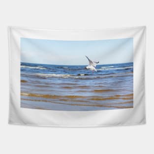 White seagull flying above the water to the left with its wings open Tapestry