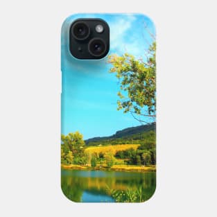 Scene with a green tree hanging above the waters of the lake with vegetation on its shores and Marche hills in the background Phone Case