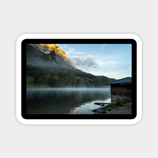 Misty Lake Portrait wide angle with boathouse. Amazing shot of a wooden house in the Ferchensee lake in Bavaria, Germany, in front of a mountain belonging to the Alps. Scenic foggy morning scenery at sunrise. Magnet by EviRadauscher