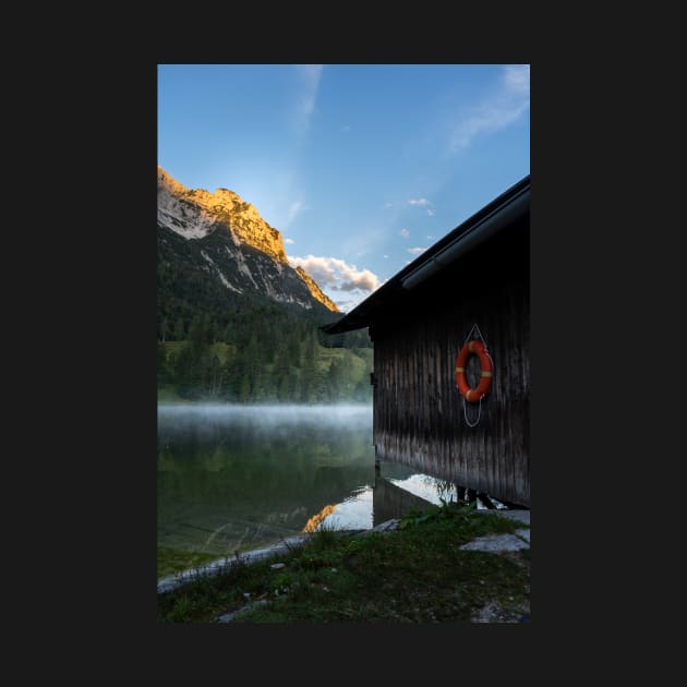 Boathouse with lifesaver Portrait. Amazing shot of a wooden house in the Ferchensee lake in Bavaria, Germany, in front of a mountain belonging to the Alps. Scenic foggy morning scenery at sunrise. by EviRadauscher