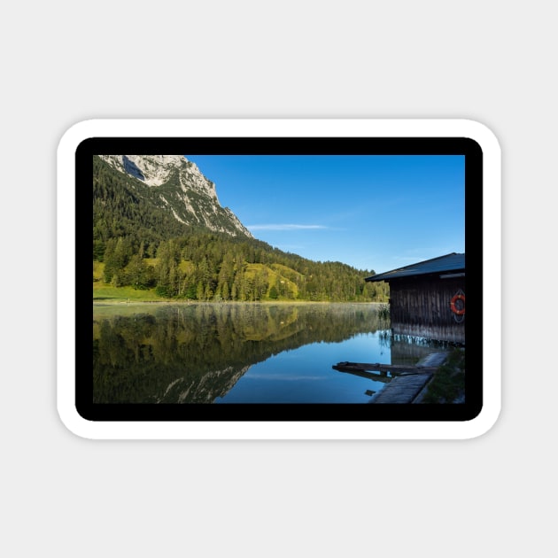 Lake water reflections with wooden boathouse wide angle. Amazing shot of a wooden house in the Ferchensee lake in Bavaria, Germany, in front of a mountain belonging to the Alps. Magnet by EviRadauscher