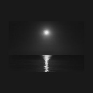 A grayscale shot of a boat in the calm sea with the reflection of the moon at night T-Shirt