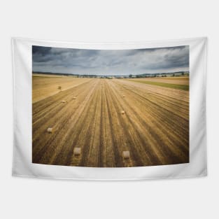 Aerial view of round hay bales on stubble with a village in the background Tapestry