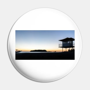 Silhouetted against golden glow of sunrise lifesafers lookout on Mount Maunganui beach New Zealand. Pin