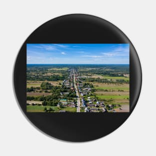 Aerial view of village surrounded by agricultural fields under blue sky Pin