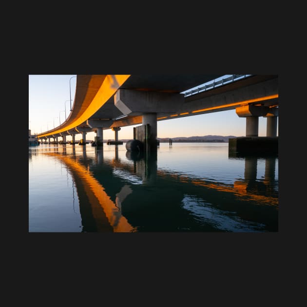 Morning sun strikes side Tauranga Harbour Bridge in golden hue reflected leading lines into calm water below by brians101