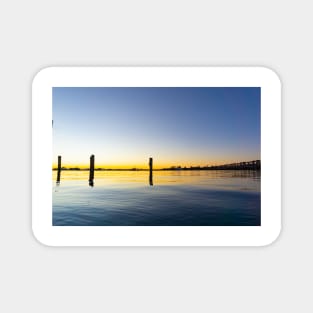 Sweeping lines of Tauranga's historic railway bridge with sunrising on left cast golden hues across harbor Magnet