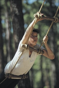 A teenager climbs a rope ladder