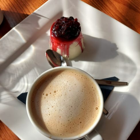 Creamy coffee topped with froth, paired with a smooth panna cotta drizzled with red berry compote and garnished with whole berries.