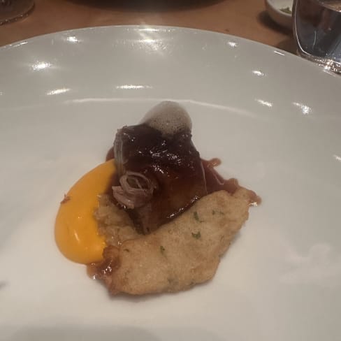 Carne estofada en salsa oscura, acompañada de puré de naranja cremoso y una espuma delicada, con un elemento crujiente que aporta textura.