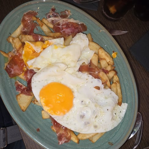 Papas fritas crujientes con bacon y un huevo frito, creando un plato abundante y satisfactorio.