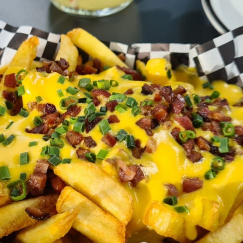 Goldene, knusprige Pommes frites mit geschmolzenem Käse, garniert mit knusprigem Speck und frischen, gehackten Frühlingszwiebeln.