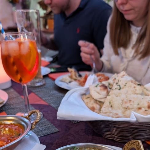 Schüssel mit reichhaltigem Saag Paneer, bestehend aus würfeligem Käse in cremiger Spinatsoße, garniert mit Sahne und frischem Koriander, serviert mit warmem Naan-Brot.