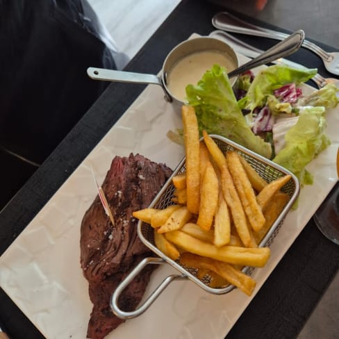 Servie de tranches de viande de boeuf tendre, accompagnée de frites croustillantes et d'une salade fraîche, avec une petite sauce crémeuse pour accompagner le plat.