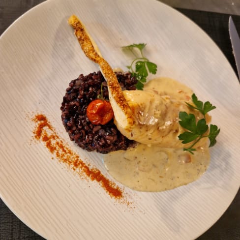 Un morceau de poulet tendre, servi avec une sauce crémeuse aux herbes, garni de persil et d'une tomate cerise. Accompagné d'un tas de riz noir au goût noisette, saupoudré de paprika.