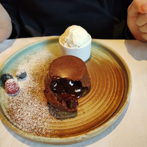 En lyxig chokladlava-kaka med en mörk, sprucken yta som avslöjar ett rinnande chokladfyllning, pudrad med florsocker och serverad med en kula vaniljglass samt färska bär.