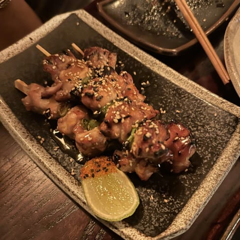 Grilled chicken skewers glazed with teriyaki sauce, topped with sesame seeds and served with a lime wedge.