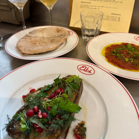 Plat de légumes grillés, avec des herbes fraîches et des graines de grenade, accompagné de pain plat légèrement grillé.