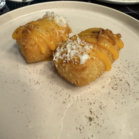 Croquetas doradas con salsa de queso y queso desmenuzado, sazonadas con especias.