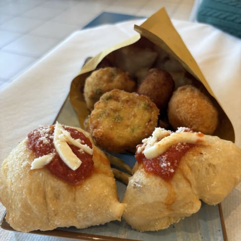 Una deliziosa selezione di antipasti con ravioli dorati ripieni, salsa di pomodoro e formaggio, accompagnati da crocchette croccanti con erbe verdi.
