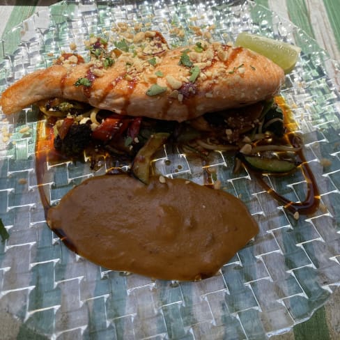 Filete de salmón perfectamente cocido, con un crujiente de nueces o cebollas fritas, acompañado de una mezcla colorida de verduras salteadas y una salsa oscura.