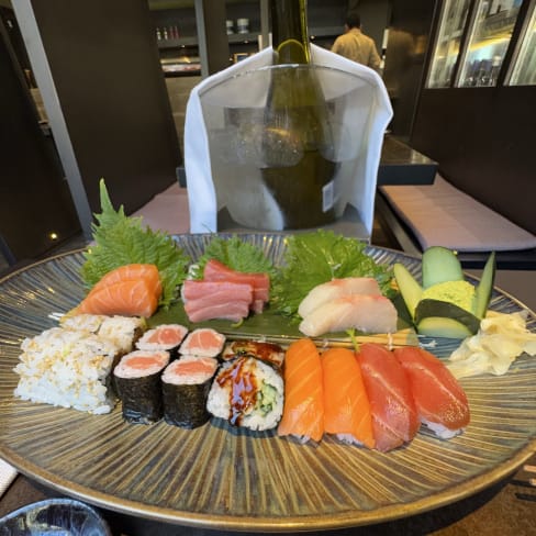 Plato de sushi variado con sashimi de salmón y atún, rollos de mariscos, hojas de shiso y wasabi.