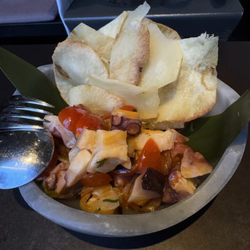 Mezcla colorida de pulpo y tomates frescos, acompañada de crujientes chips de plátano.