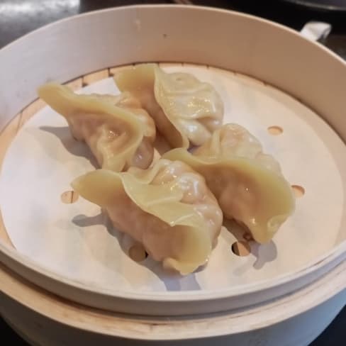 Dumplings delicados envueltos en masa translúcida, rellenos de carne y verduras, presentados en una vaporera de bambú.