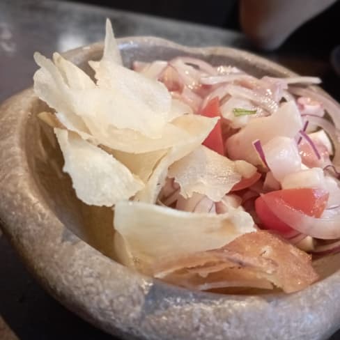 Ensalada fresca y colorida con verduras en rodajas finas, como cebolla roja y tomate, acompañada de chips crujientes.