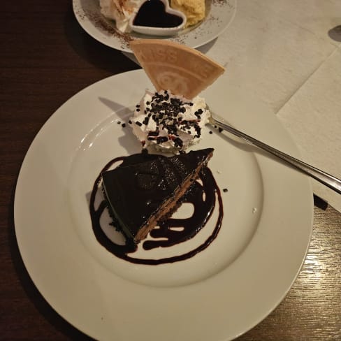 Twee desserts: een rijke chocoladetaart met slagroom en donkere chocoladesaus, en een bolletje romige vanille-ijs met een hartvormig chocolaatje en een decoratieve wafel.