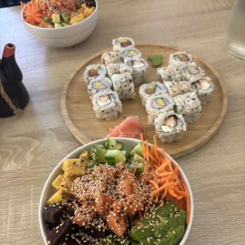 Bol généreux de légumes frais avec avocat, carottes râpées et saumon mariné, garni de graines de sésame. En arrière-plan, assortiment de sushis variés avec concombre et poisson, accompagné de gingembre mariné.