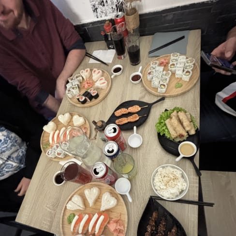 Variété de sushis et de plats japonais, incluant nigiri avec poisson frais, maki enroulés d'algues, rouleaux de printemps croustillants, et brochettes de viande grillée, le tout accompagné de sauces et condiments.