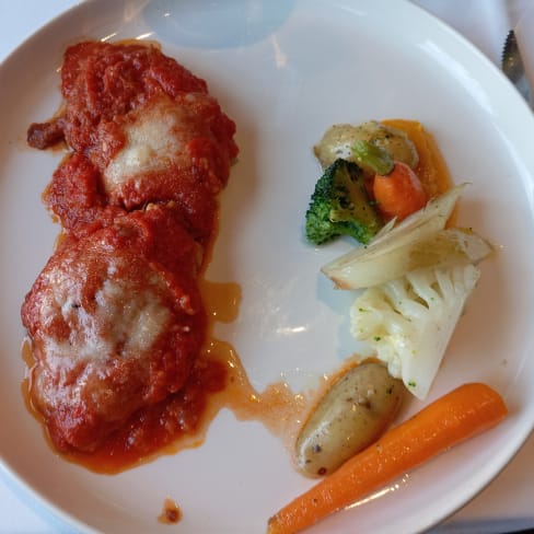 Plat de poulet pané, nappé d'une sauce tomate épaisse et de fromage fondu, accompagné de légumes sautés et de pommes de terre rôties.