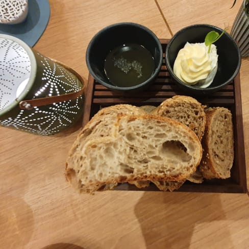 Auswahl an frisch gebackenem Brot mit knuspriger Kruste und luftiger Textur, serviert mit cremiger Butter mit Limettenzesten und einem dunklen, kräuterinfundierten Öl zum Dippen.