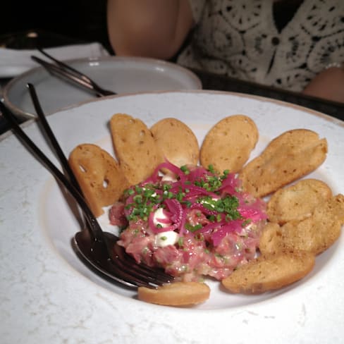 Carne crua finamente picada, guarnecida com molho cremoso e cebolas roxas em conserva, acompanhada de crostini crocantes e dourados.
