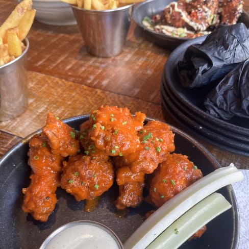 Crispy chicken pieces coated in spicy buffalo sauce, garnished with green onions, served with creamy ranch dressing and crisp celery sticks.