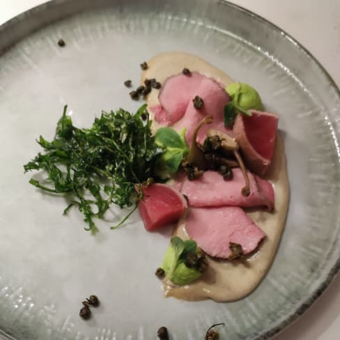 Zarte Scheiben von gepökeltem oder gekochtem Schweinefleisch auf einer cremigen Sauce, garniert mit frischen Kräutern und dunklen Kapern für einen salzigen Geschmack.