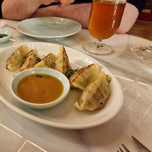Empanadillas doradas y crujientes rellenas de carne y verduras, acompañadas de salsas de soja y dulce.