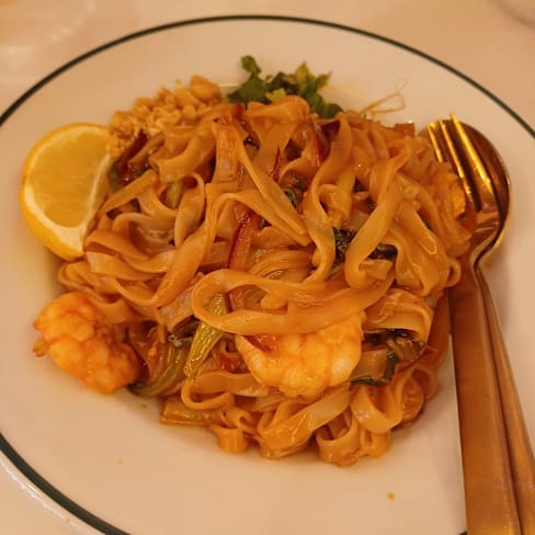 Fideos salteados con camarones y verduras coloridas, acompañados de un gajo de limón.