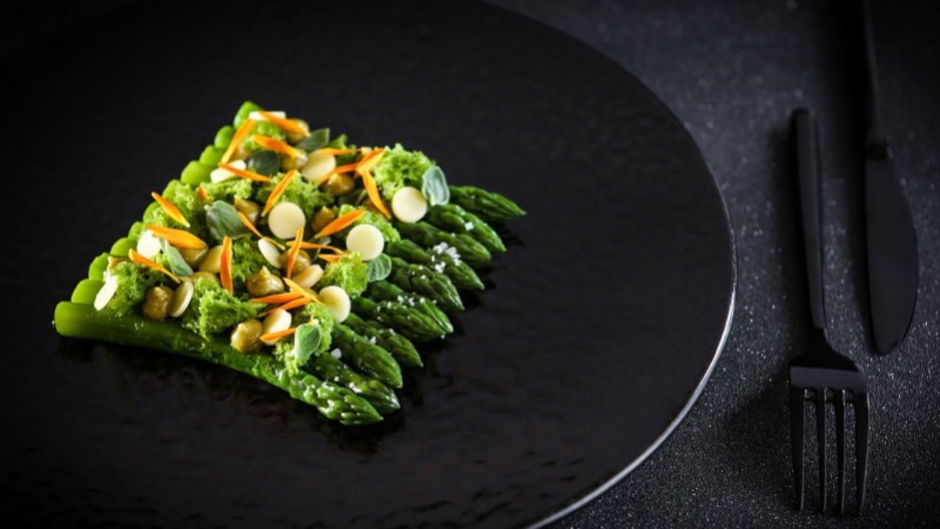 Plat élégant d'asperges vertes tendres, nappées d'une sauce verte légère, garnies de carottes en fines tranches et de graines croquantes.