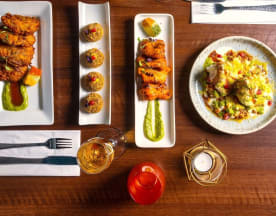 Crispy chicken wings glazed with rich sauce and green herb drizzle, golden-brown fritters garnished with red and green bits, and a colorful rice dish mixed with diced vegetables.