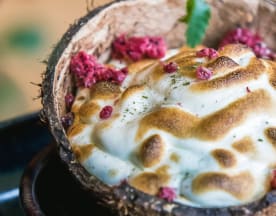 Sobremesa única servida numa casca de coco, com cobertura de merengue tostado de tom dourado, contrastando com uma base cremosa e decorada com pedaços de framboesas secas.