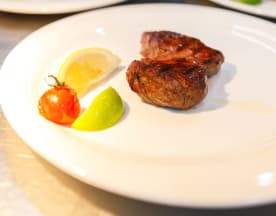 Um pedaço de carne grelhada, suculenta e tenra, com uma crosta castanha rica, acompanhado de fatias de limão e lima, e um tomate-cereja assado que acrescenta um toque de doçura.