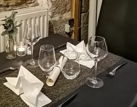 Table élégamment dressée avec une nappe sombre, des verres polis, des serviettes pliées en triangle, une petite vase de verdure et une bougie allumée pour une ambiance chaleureuse.